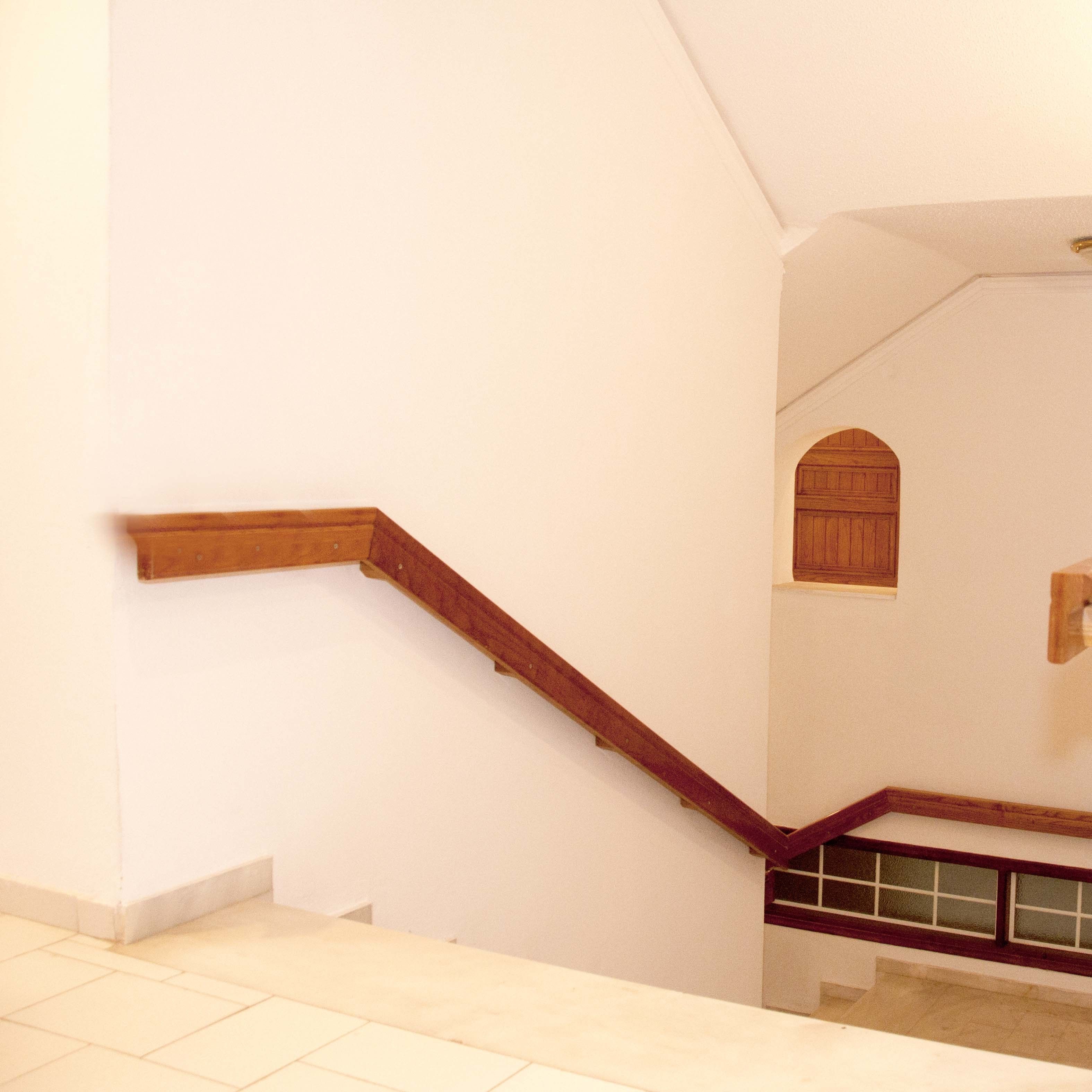 A staircase with wooden handrails and a white wall.