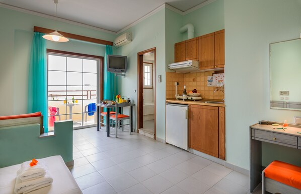 A compact room with a dining area, kitchenette, and a window with curtains. - Louladakis Apartments (Platanias)