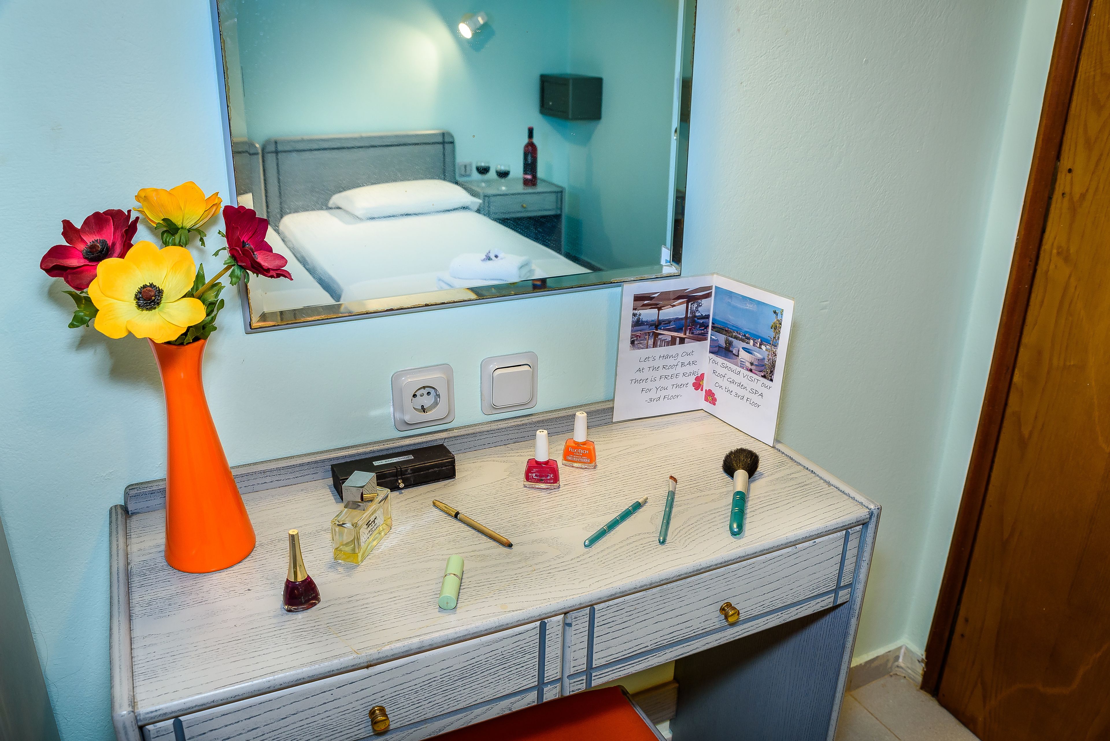 A hotel room vanity with a mirror, a vase of flowers, and various toiletries.