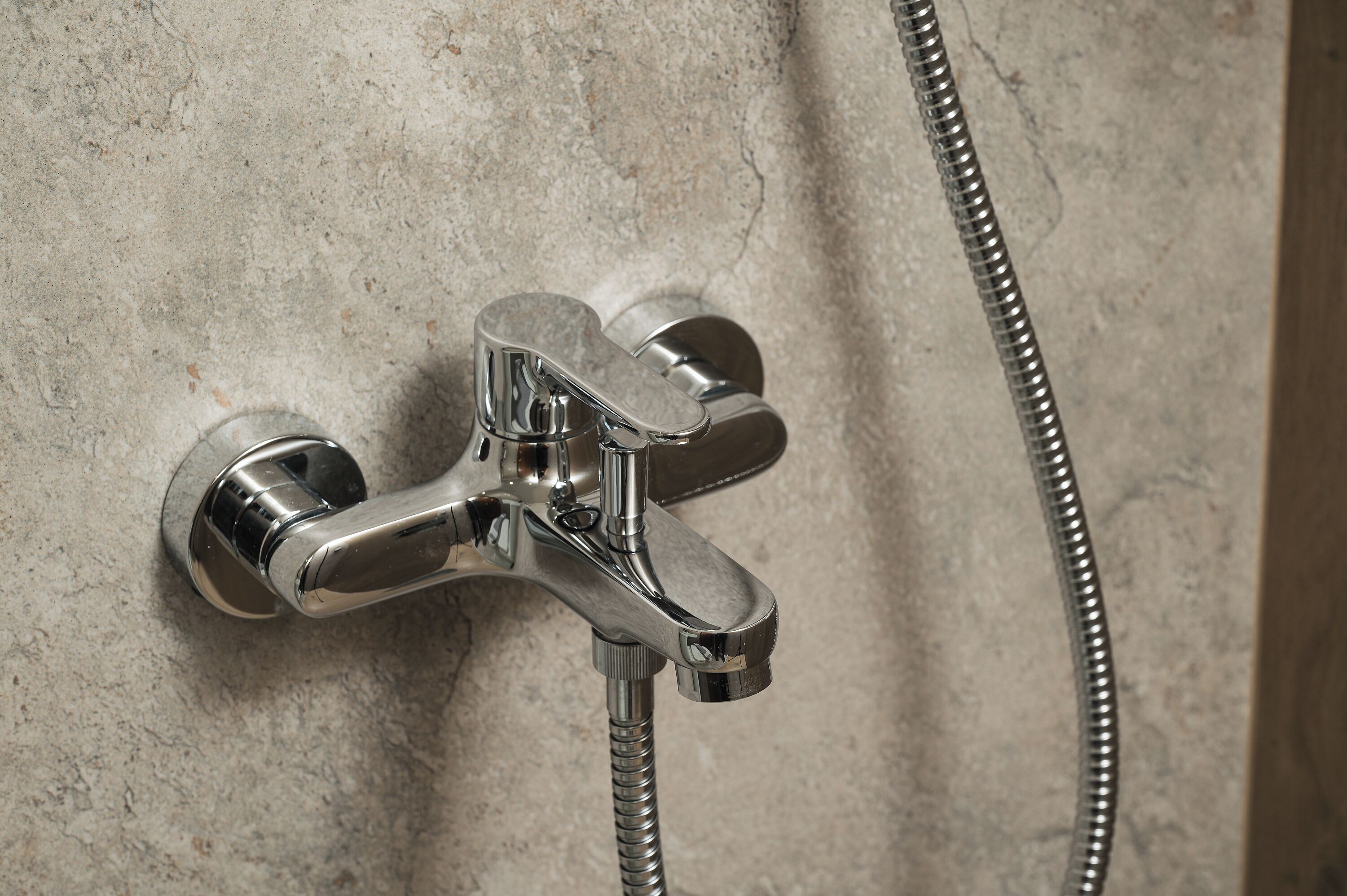 A chrome shower faucet with a flexible hose attached, mounted on a textured wall.