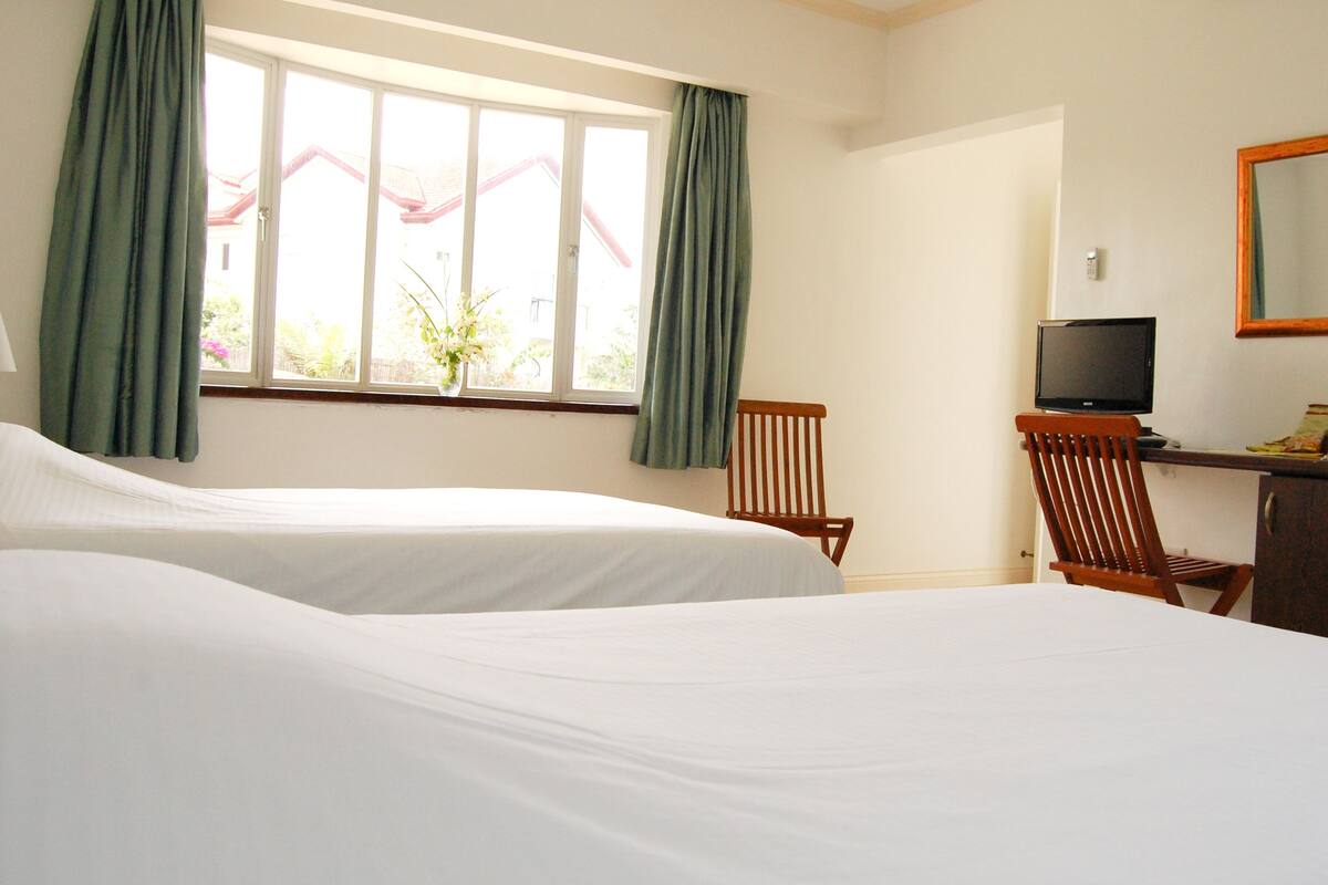 A hotel room with two beds, a desk with a television, a chair, and a window with curtains.