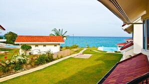 Vista desde un balcón sobre una piscina, una casa con techo rojo y el océano.