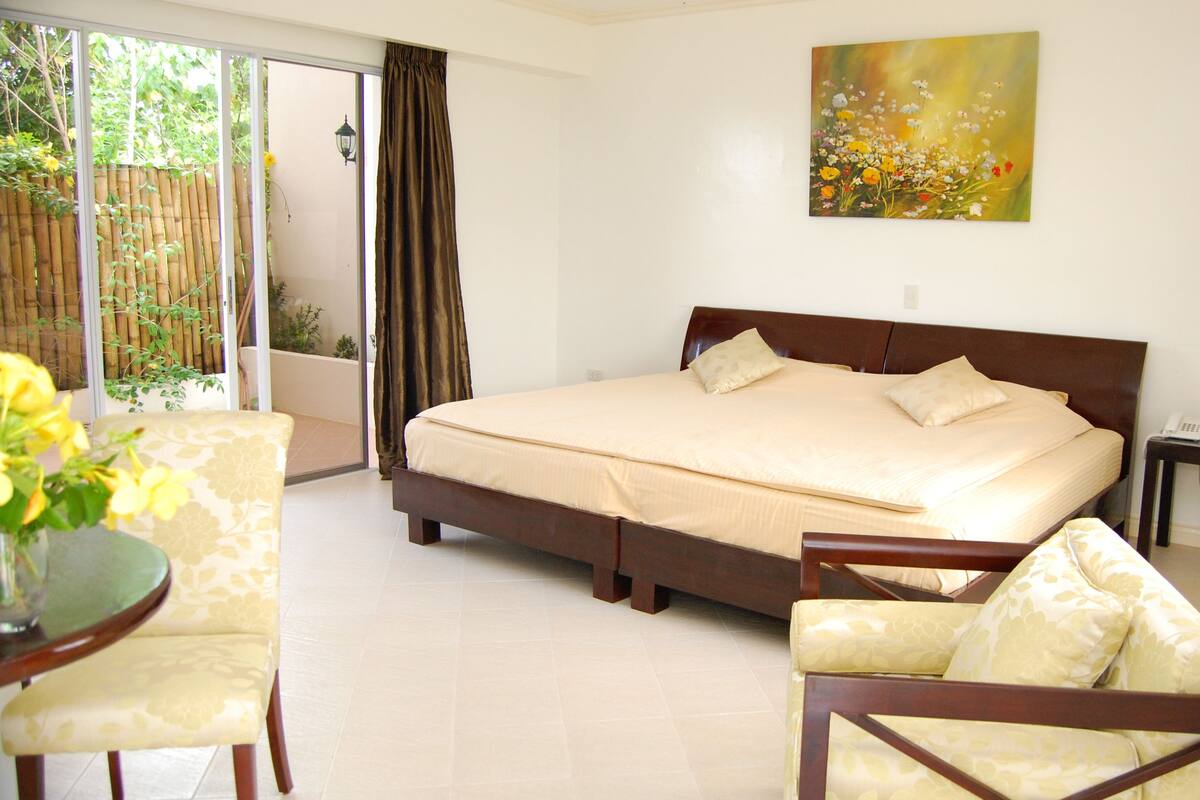 A bedroom with a large bed, a chair, a small table, and a painting on the wall.