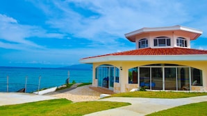 Una casa costera con techo de tejas rojas, amplios ventanales y vista al mar.