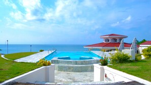 A swimming pool with a view of the ocean, a red-roofed building, and a grassy area. - Sherwood Bay Resort & Aqua Sports (Dauis)