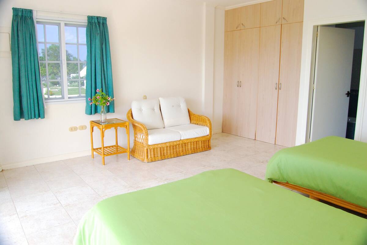 A bedroom with a wicker sofa, a green bed, a wooden wardrobe, and a window with curtains.