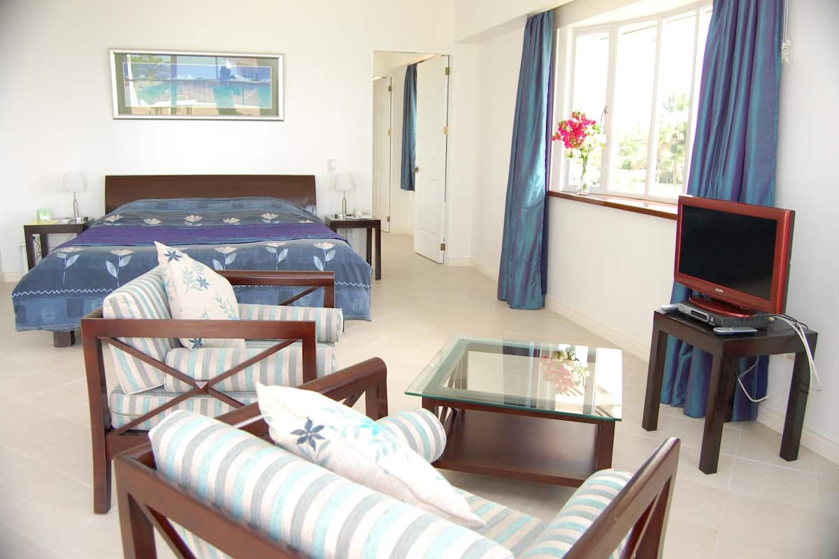 A hotel room with a bed, a sofa, a glass coffee table, a TV, and a window with curtains.