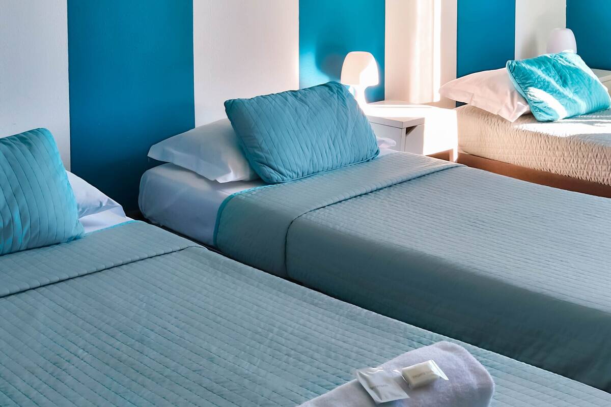 Een hotelkamer met twee bedden, elk met een blauwe geborduurde sprei en bijpassende kussens. Er staat een witte nachtkastje met een lamp en een klein tafeltje naast de bedden.