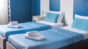 Een hotelkamer met twee bedden, elk met blauw beddengoed en witte kussens, een schilderij aan de muur en een witte lamp op een nachtkastje.