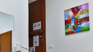 Een trap met houten treden die leidt naar een deur, met een bordje, een aan de muur hangend schilderij en een witte muur met een stopcontact.