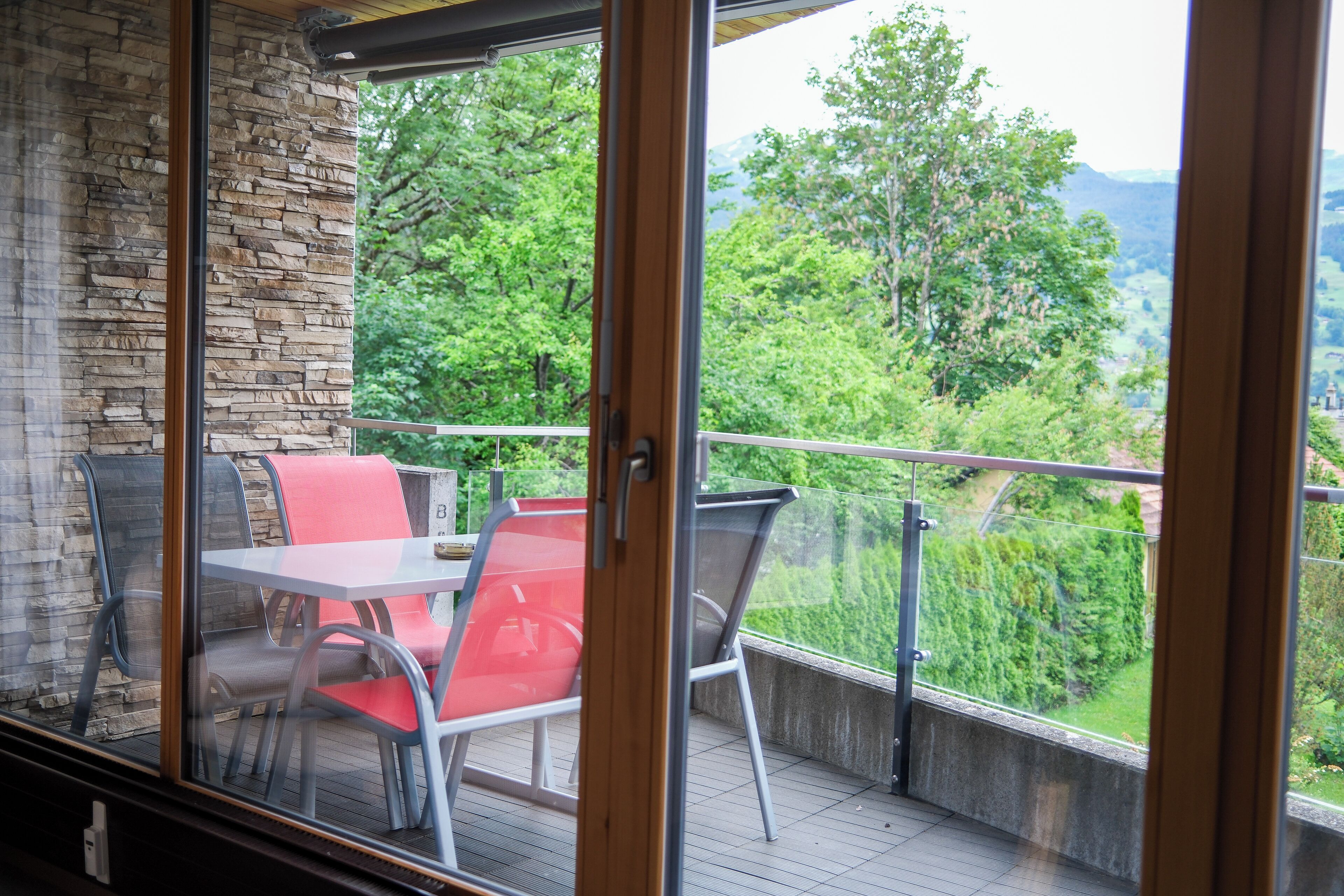 Un balcon avec une table et des chaises, un mur en pierre et une vue sur la verdure et les montagnes.