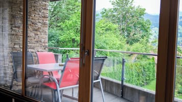 Un balcon avec une table et des chaises, un mur en pierre et une vue sur la verdure et les montagnes.