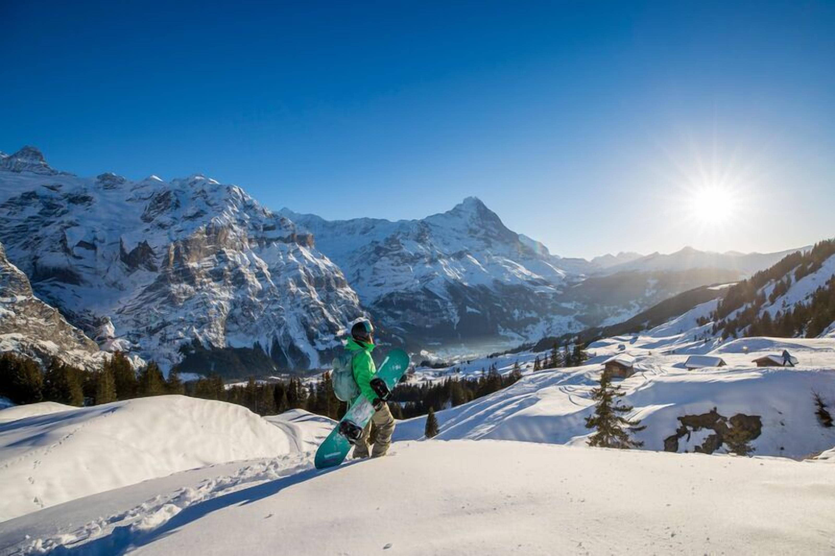 A snowboarder on a snowy mountain with a clear sky and sun shining.