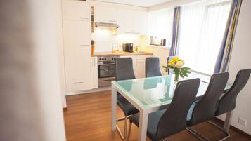A modern kitchen with white cabinets, stainless steel appliances, and a glass dining table with four chairs.