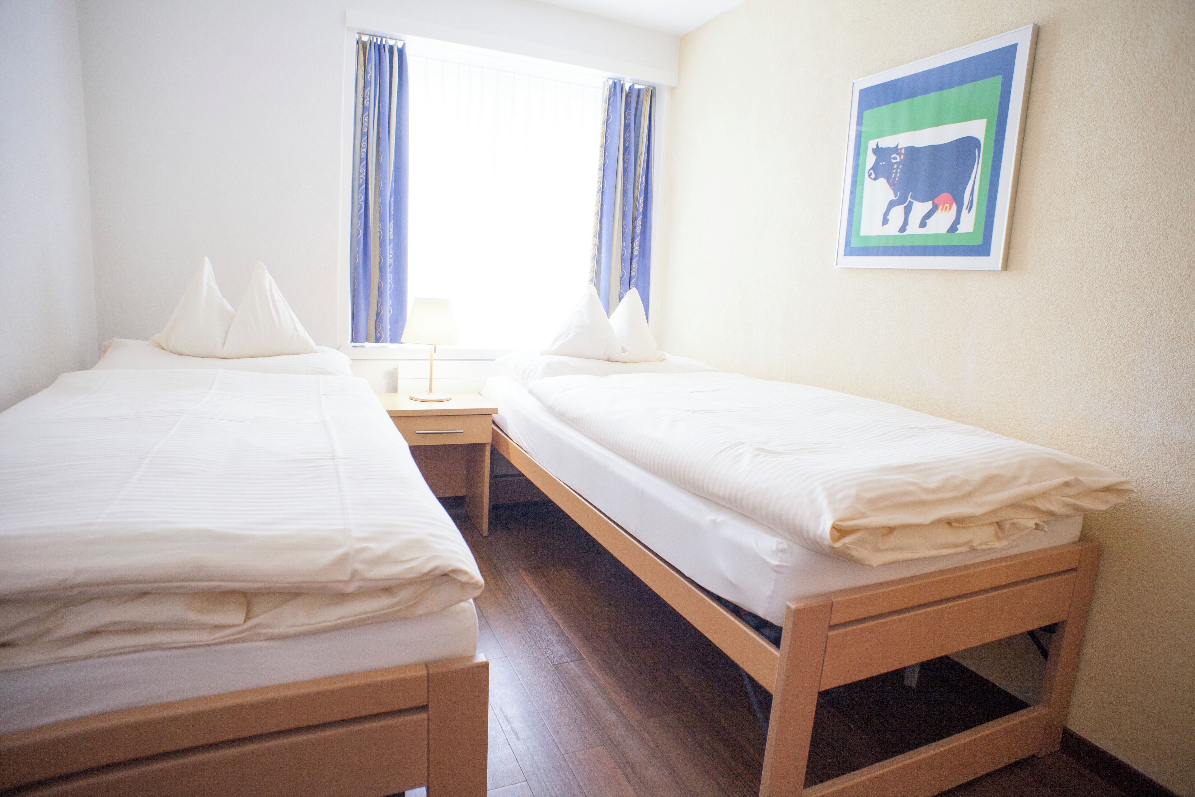 A room with two single beds, a nightstand, and a window with curtains.
