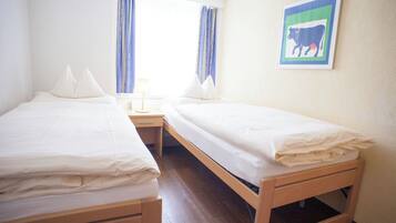 A room with two single beds, a nightstand, and a window with curtains.