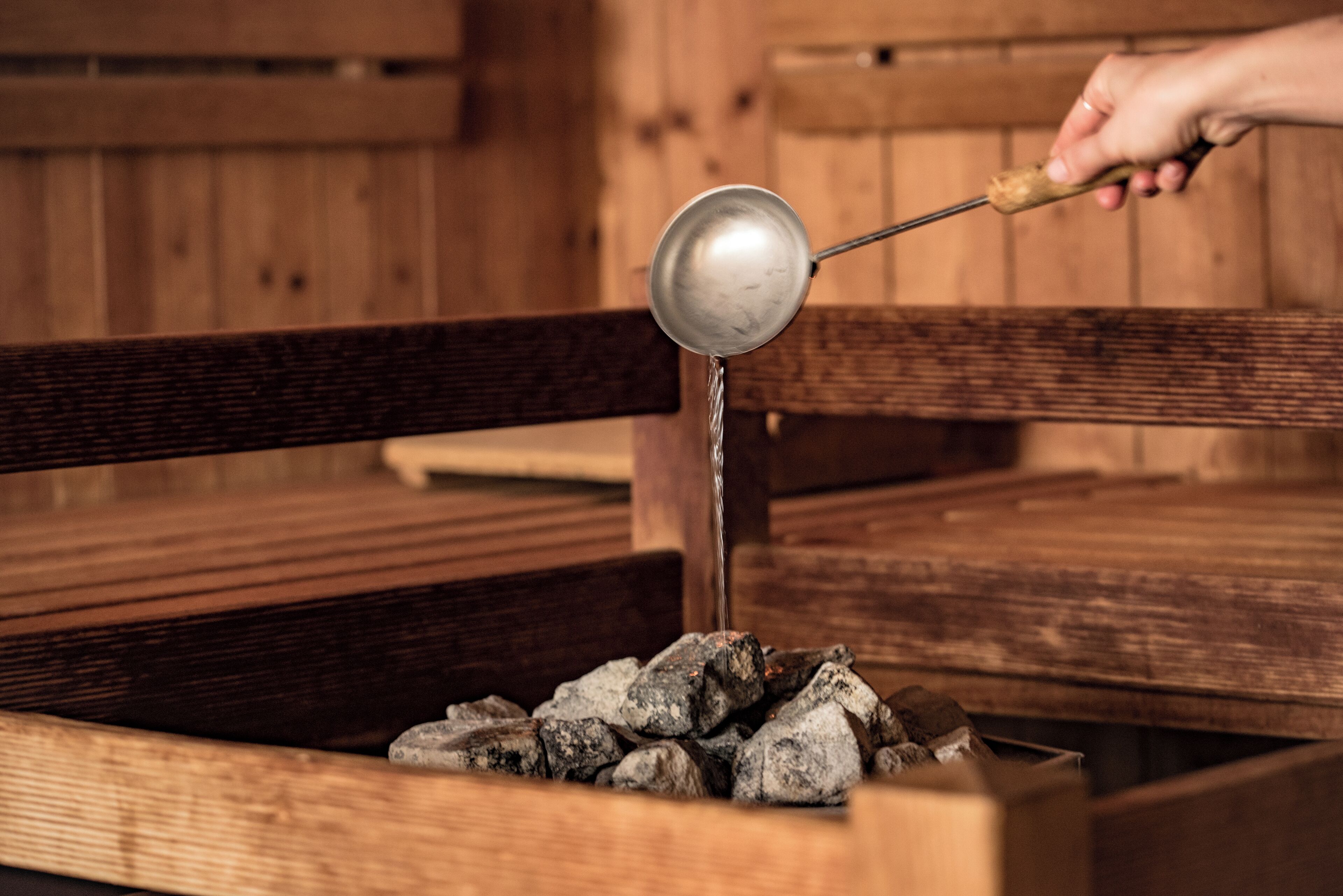 A wooden bench with a metal ladle pouring water over rocks.