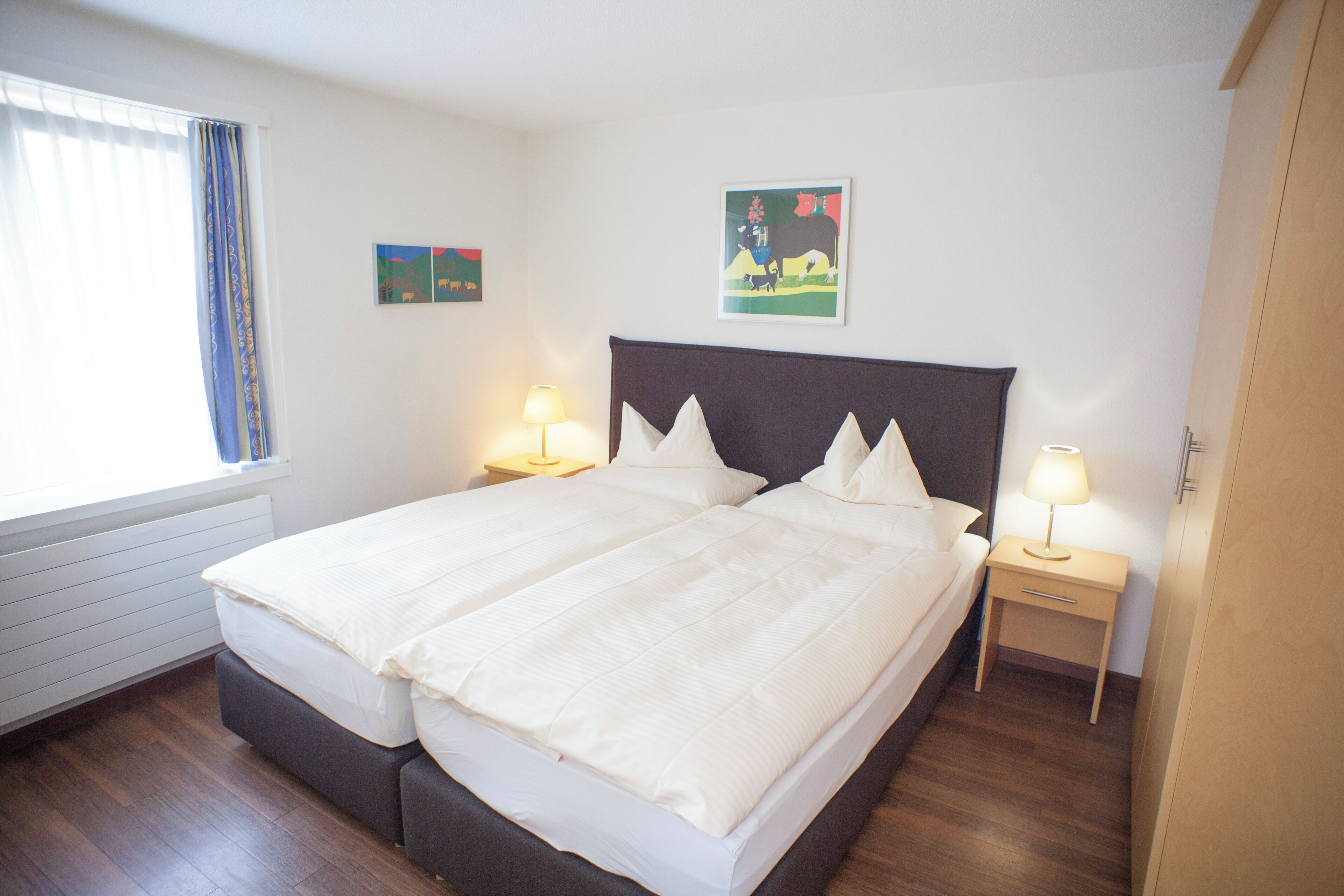 A double bed with a dark headboard, two bedside tables with lamps, and two wall-mounted artworks.