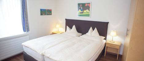 A double bed with a dark headboard, two bedside tables with lamps, and two wall-mounted artworks.