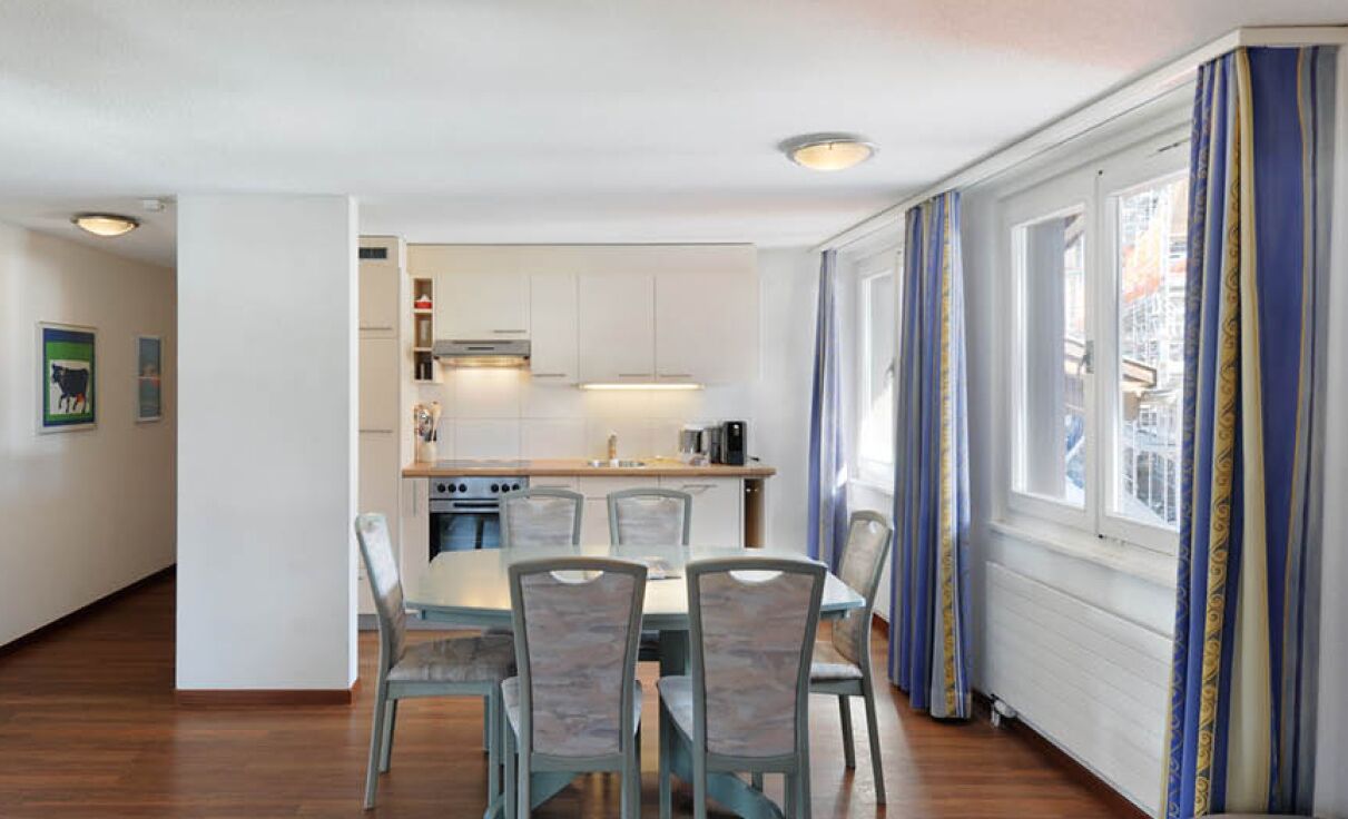 A modern kitchen with white cabinets, a dining table with chairs, and a window with curtains.