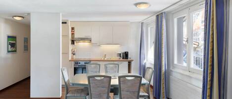A modern kitchen with white cabinets, a dining table with chairs, and a window with curtains.