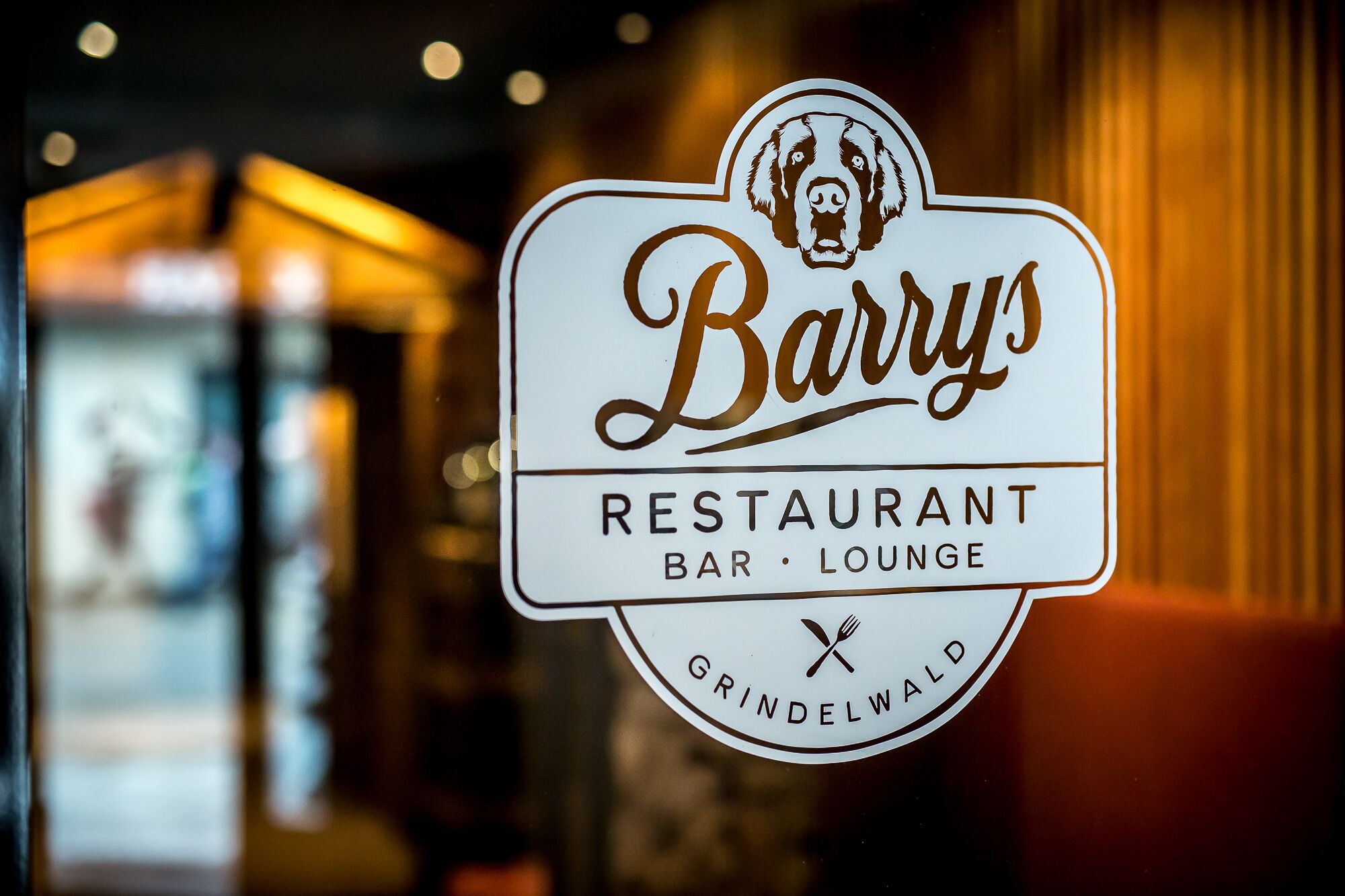 Naamplaatje voor 'Barry's Restaurant Bar Lounge Grindelwald', met een logo van een hond en gekruist bestek.