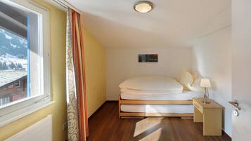 A bedroom with a bed, a nightstand, a window with curtains, a radiator, and a small painting on the wall.