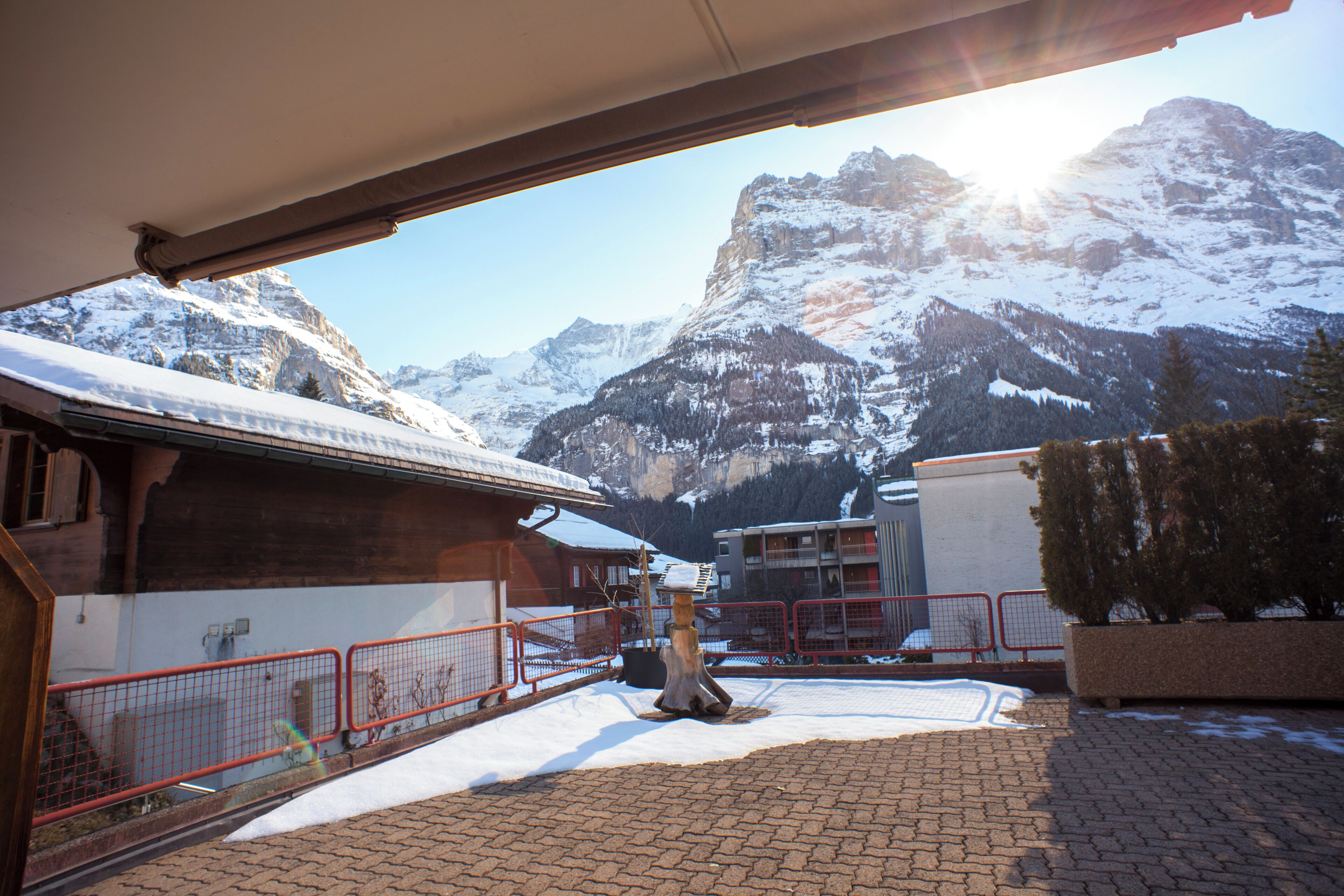 A snow-covered mountain landscape with a building and a red fence in the foreground.