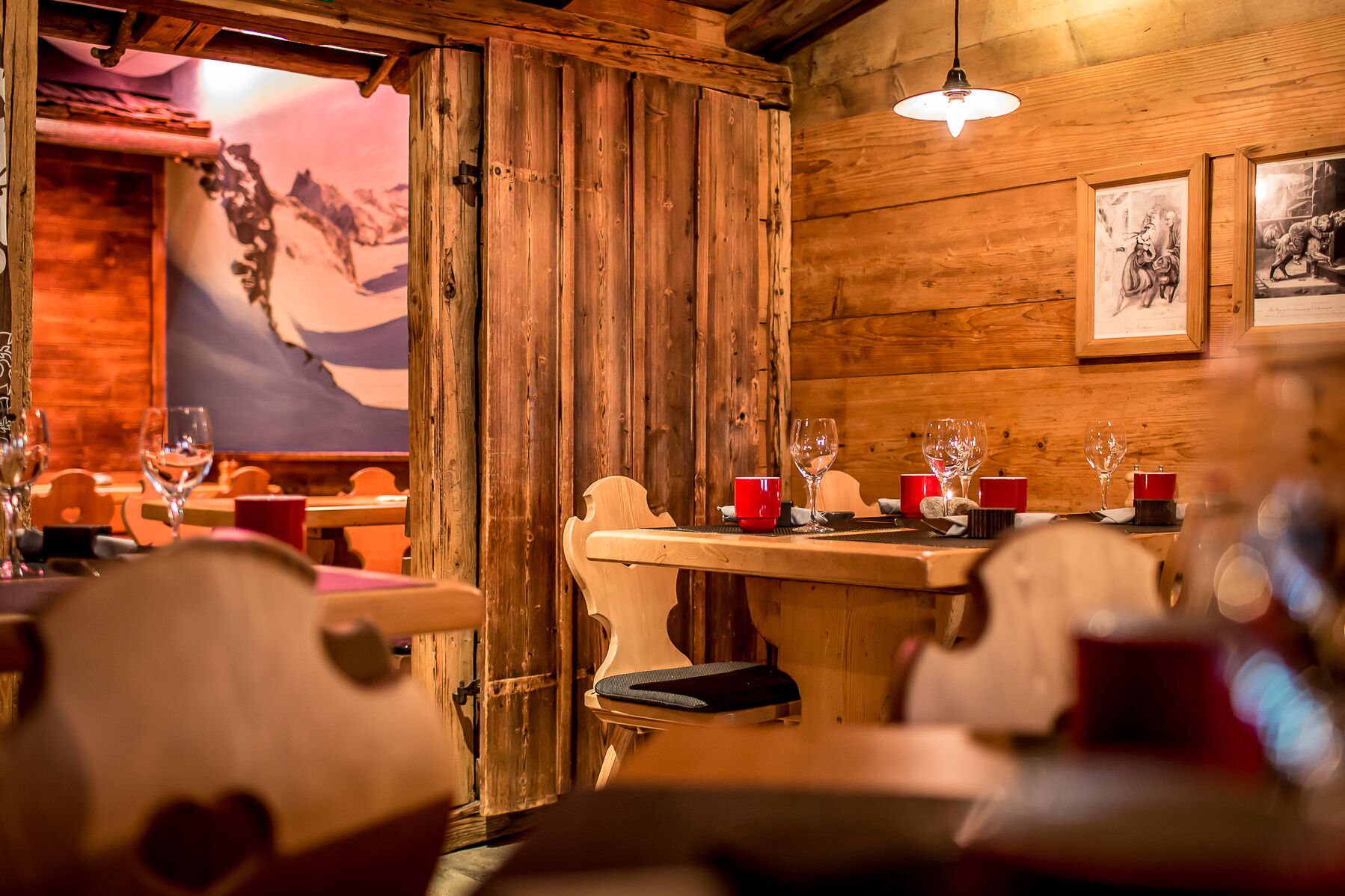 En mysig restaurang med träpanel på väggarna, en väggmålning och en bardisk med glas och röda muggar.