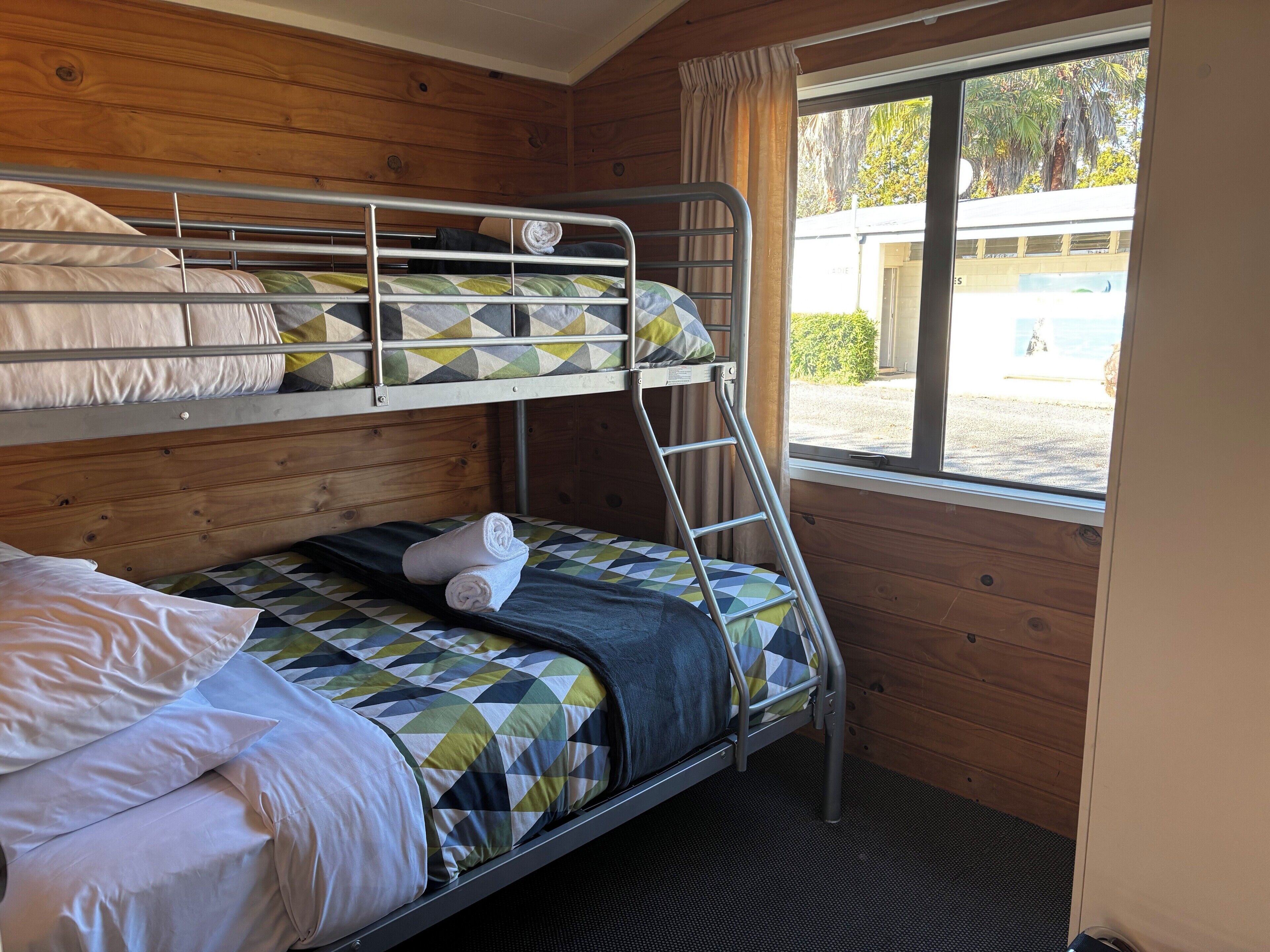 A bunk bed room with a window, wooden walls, and a view of the outside.