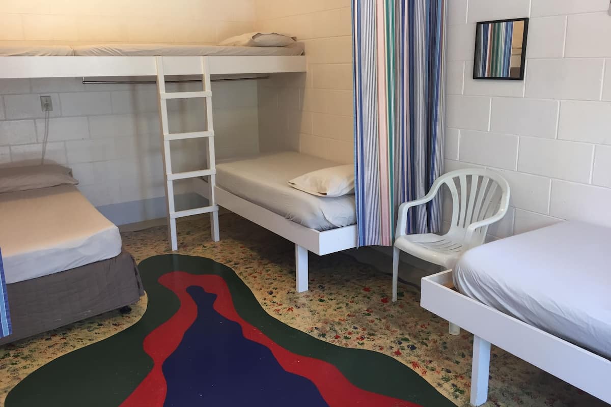 A dormitory room with bunk beds, a white chair, a ladder, and a colorful rug.