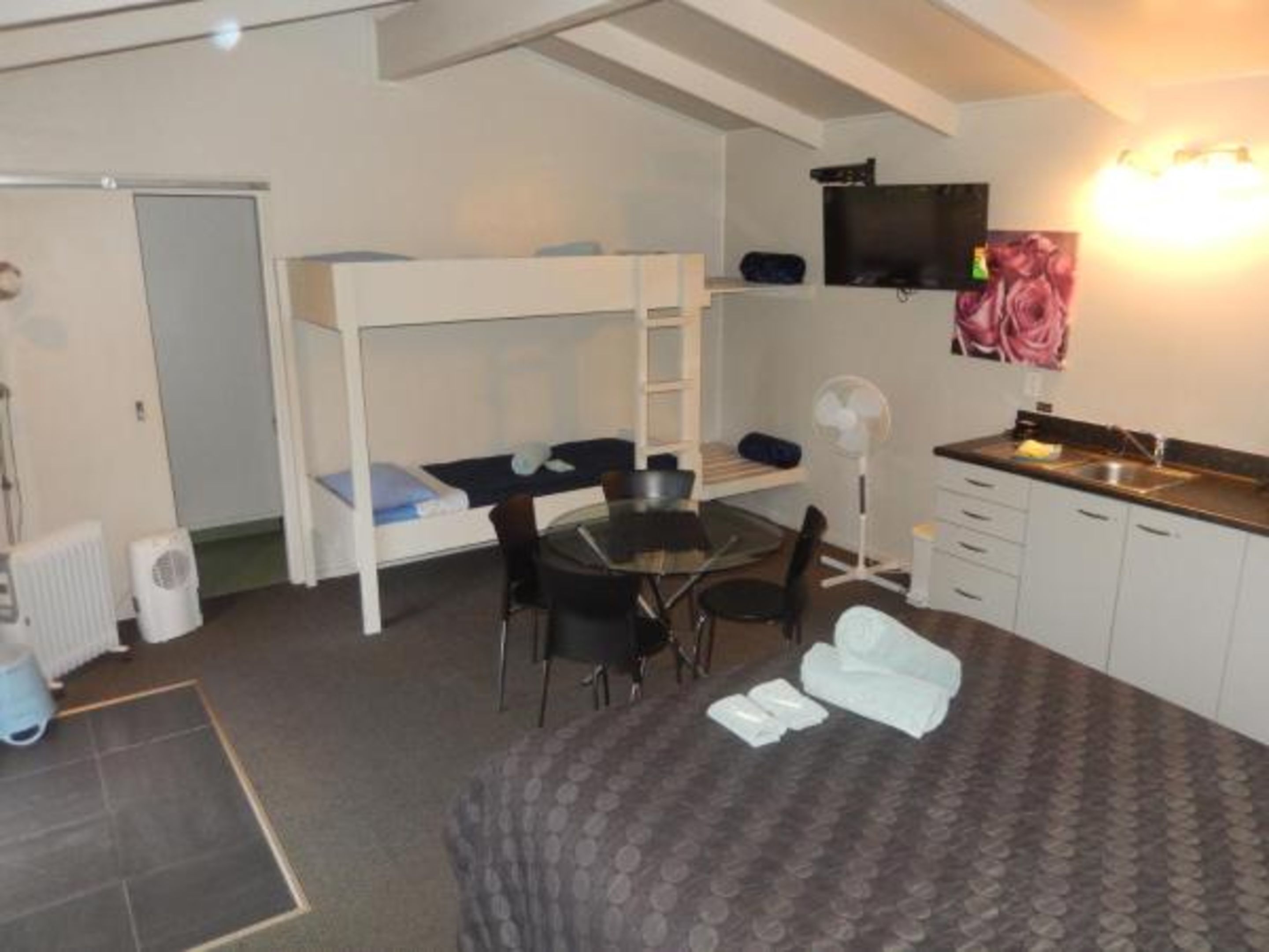 A compact room with a bunk bed, a small dining table, a chair, a fan, a sink, and a television.