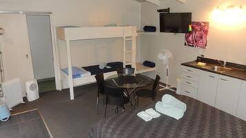 A compact room with a bunk bed, a small dining table, a chair, a fan, a sink, and a television.