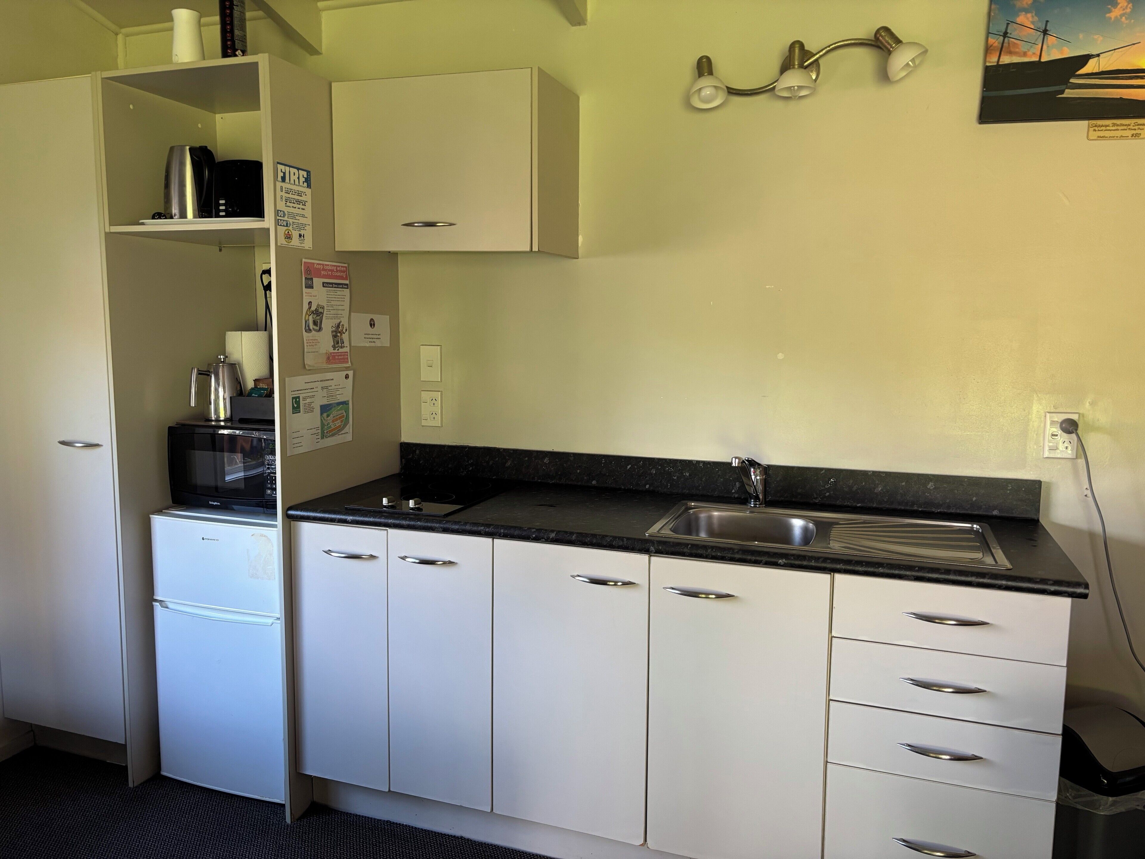 A compact kitchen with white cabinets, a black countertop, a stainless steel sink, and a microwave.