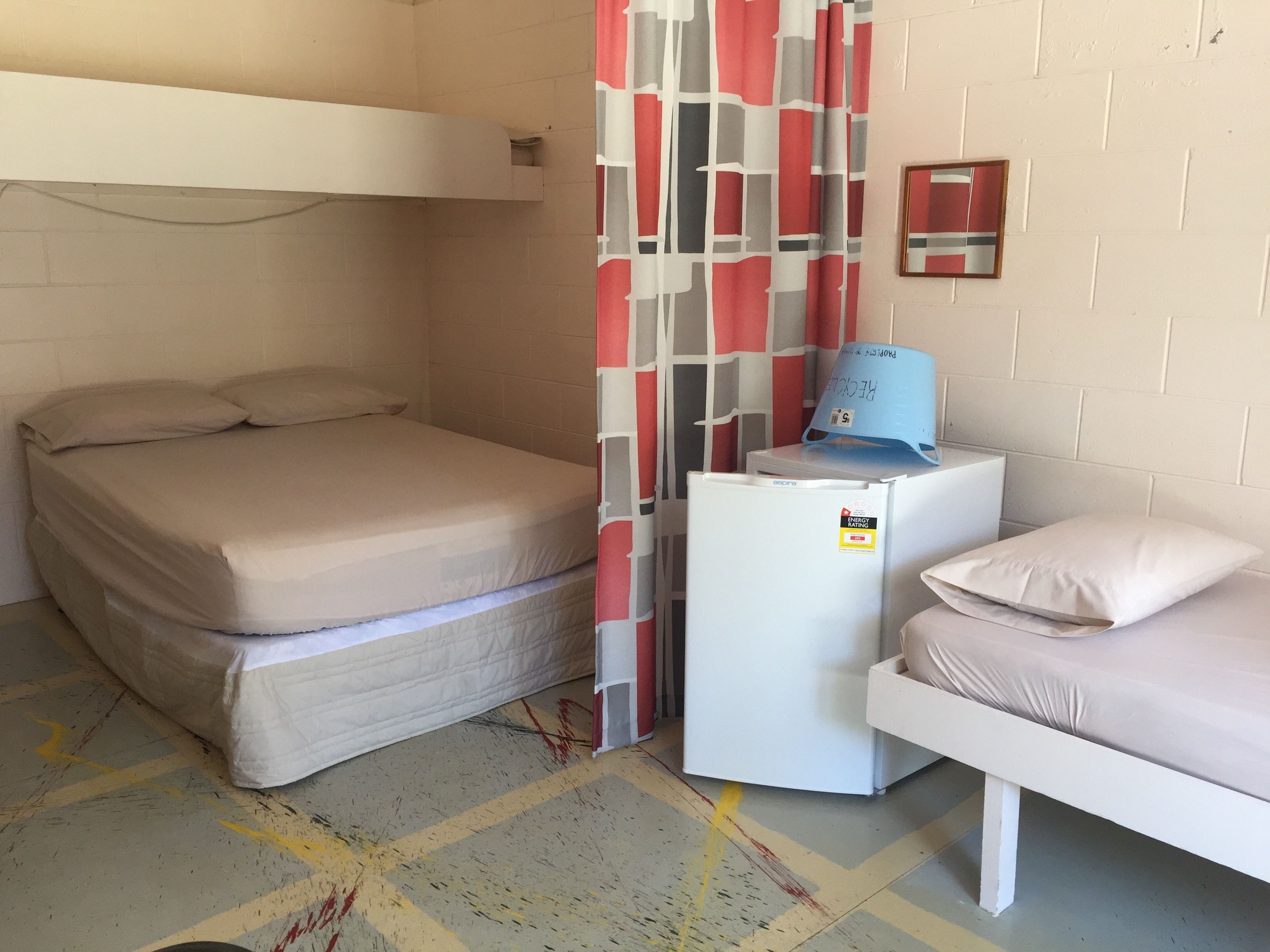 A small, compact room with a bunk bed, a single bed, a refrigerator, and a wall-mounted mirror.