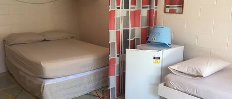 A small, compact room with a bunk bed, a single bed, a refrigerator, and a wall-mounted mirror.