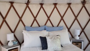 Uma cama com manta branca e azul, almofadas e um cobertor azul. Há duas mesas de cabeceira com luminárias e cestos de armazenamento.