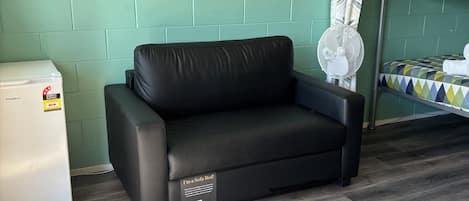 A room with a sofa bed, a small refrigerator, a bunk bed, and a wall-mounted fan.