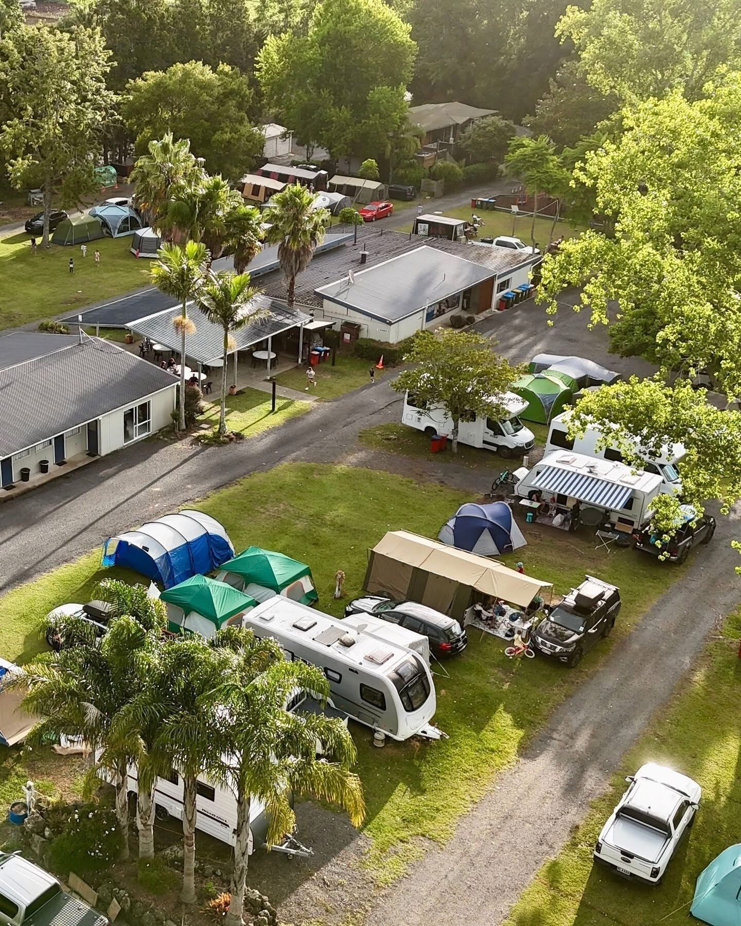 A campsite with RVs, tents, and a building with a flat roof.