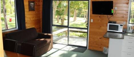 Eine Hütte mit Holzvertäfelung, einem Sofa, einem Tisch mit Papieren, einem an der Wand befestigten Fernseher und einer Küchenzeile mit einer Mikrowelle.