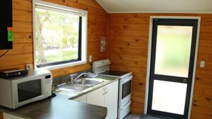Uma cozinha compacta com micro-ondas, pia e fogão, paredes de madeira e uma porta com painel de vidro fosco.