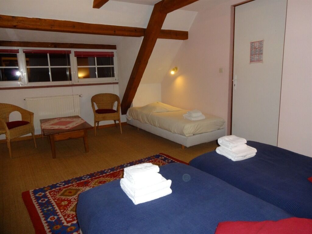 Une chambre avec deux lits, une chaise, une petite table et une fenêtre avec des stores rouges.