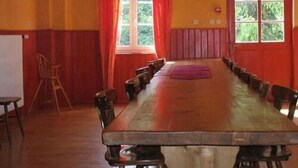 A conference room with a long wooden table, red walls, and a window with curtains. - Pension Linstant (Le Hohwald)