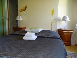 Una cama cuidadosamente tendida con un edredón oscuro, dos lámparas de noche y una pared decorada con espigas de trigo y flores.