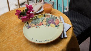 A table with a plate, a glass of orange juice, and a vase of flowers on a balcony overlooking the sea.