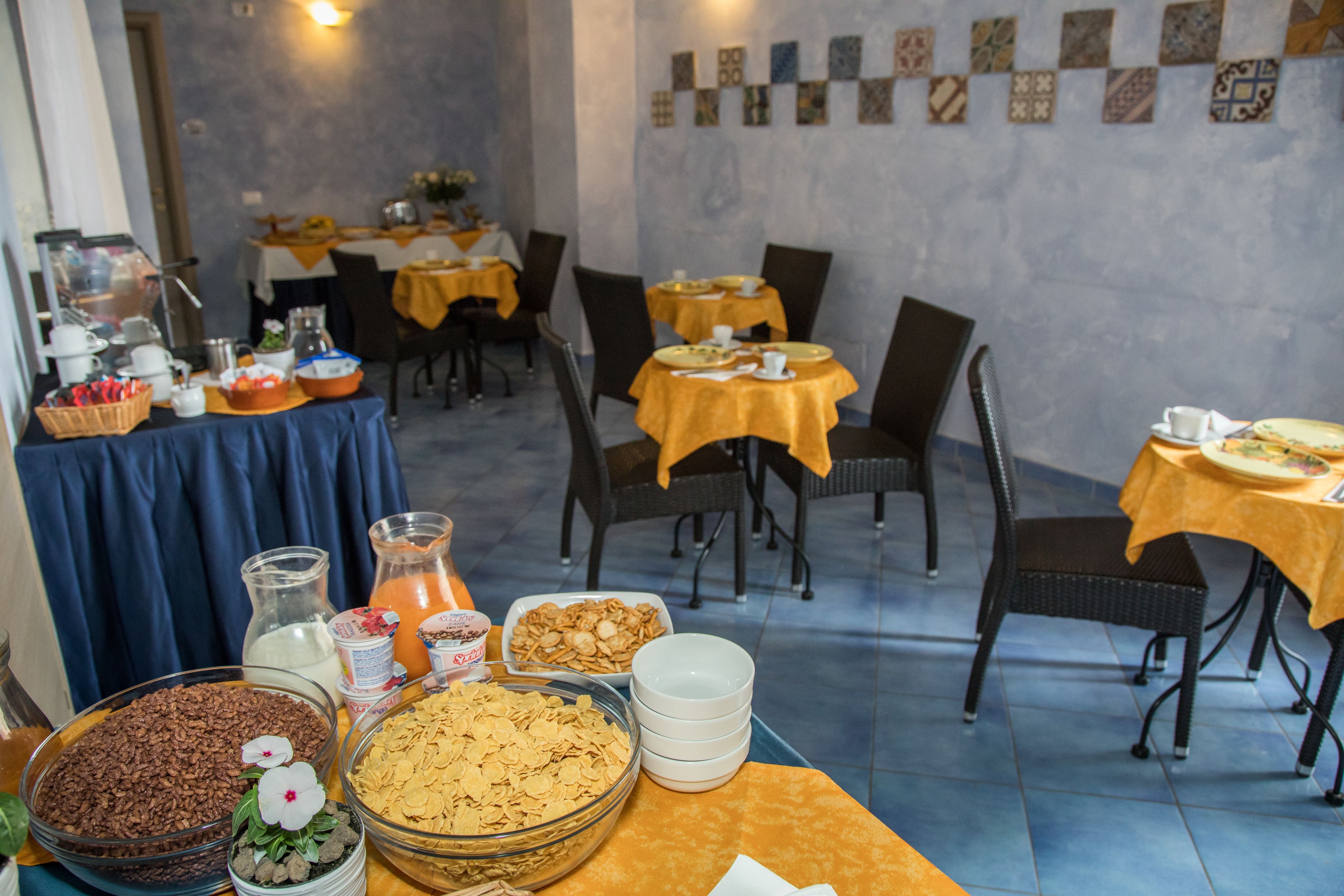 Un comedor con mesas dispuestas para el desayuno, que incluyen tazones de cereal, bollería y bebidas.