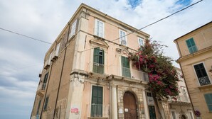 A multi-story building with a classic architectural style, featuring a central entrance with an arched doorway, green shutters, and a balcony with a metal railing.