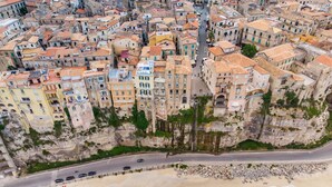 An aerial view of a coastal town with buildings built on cliffs overlooking a beach and the sea.