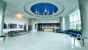 Eine geräumige Lobby mit hoher Decke, einem Empfangsbereich, einer blauen Sofaecke und einem großen Fenster, das für natürliches Licht sorgt.