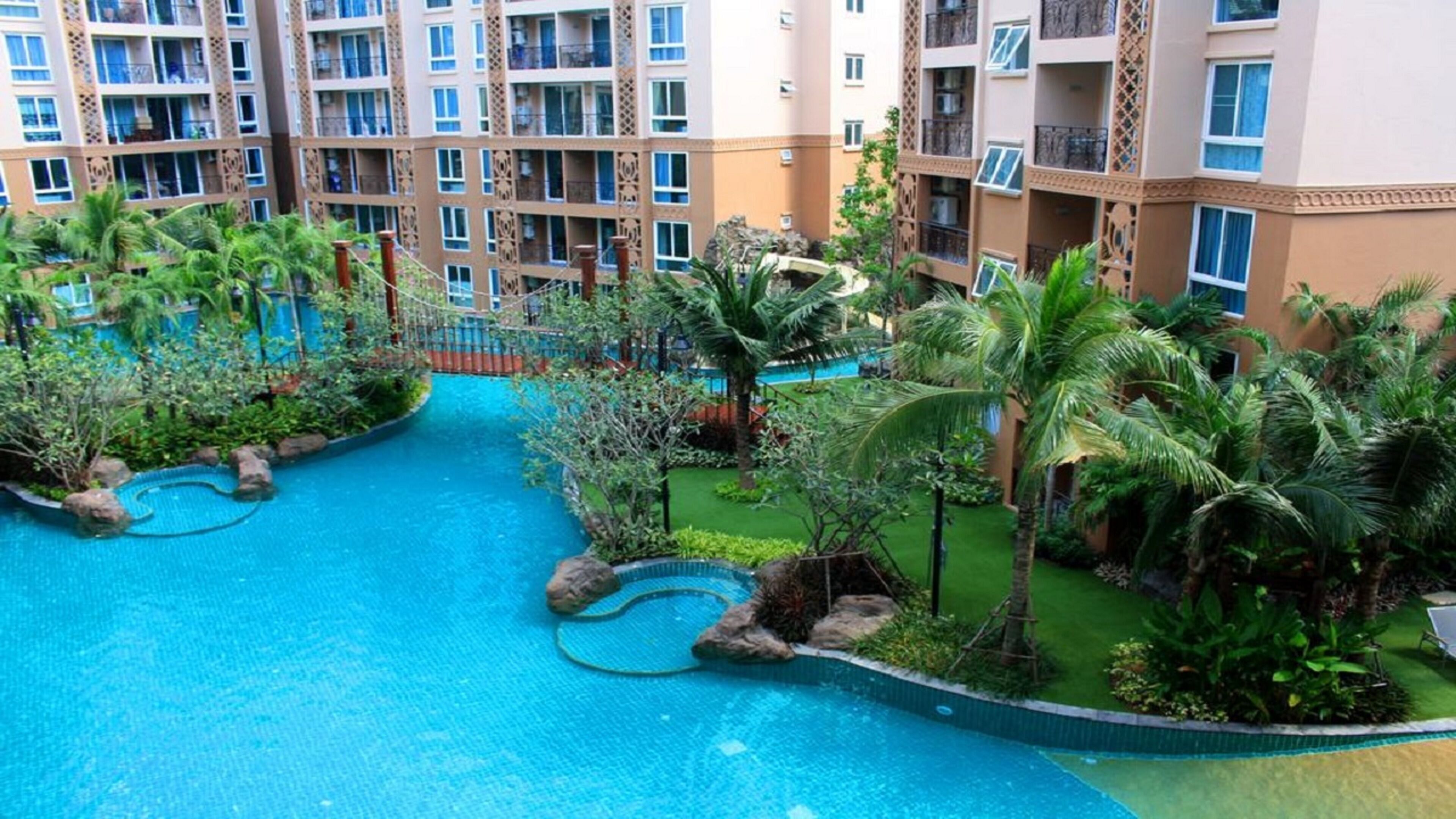 A hotel courtyard with a swimming pool, palm trees, and a bridge.
